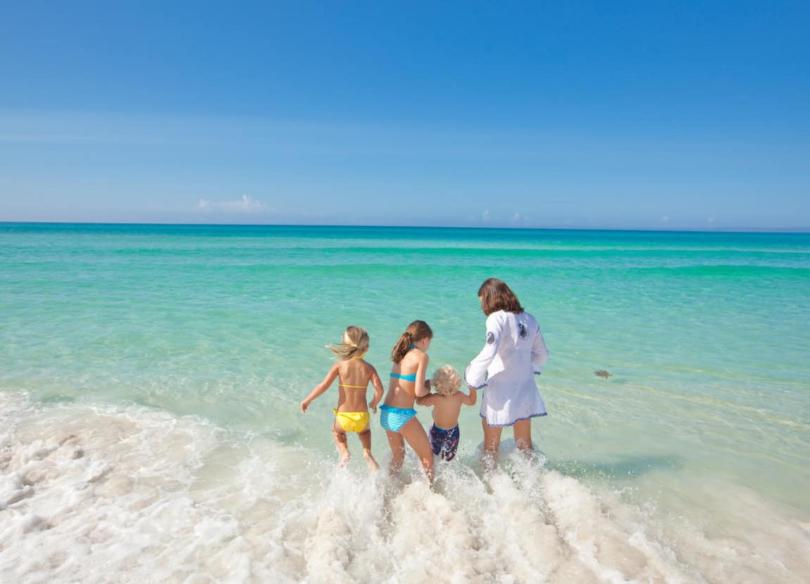 A family with young children play in the surf in the stunning emerald green waters of Northwest Florida's Gulf Coast.