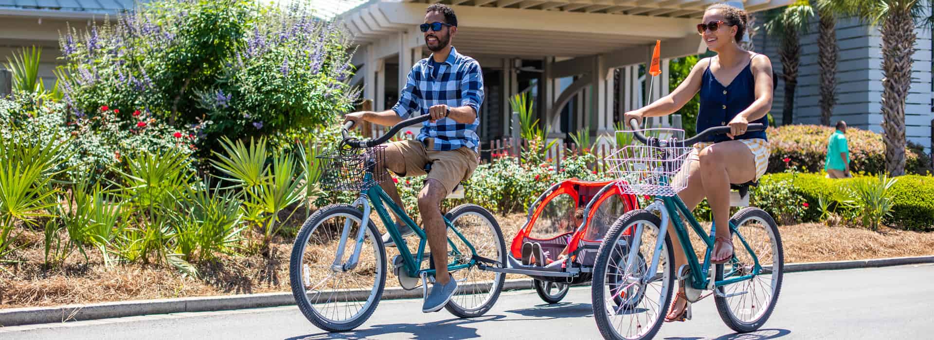 A happy couple with a child ride bicycles in front of Watercolor Inn along scenic 30A by the beach.
