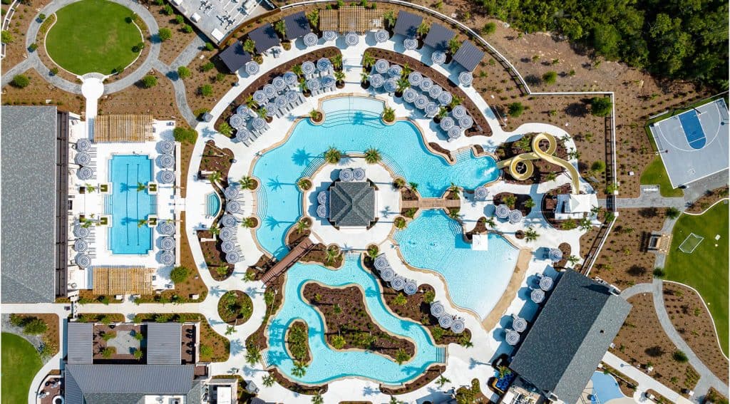 Aerial view of a large resort pool complex with winding pools, cabanas, lounge chairs, a basketball court, and surrounding landscaped areas.