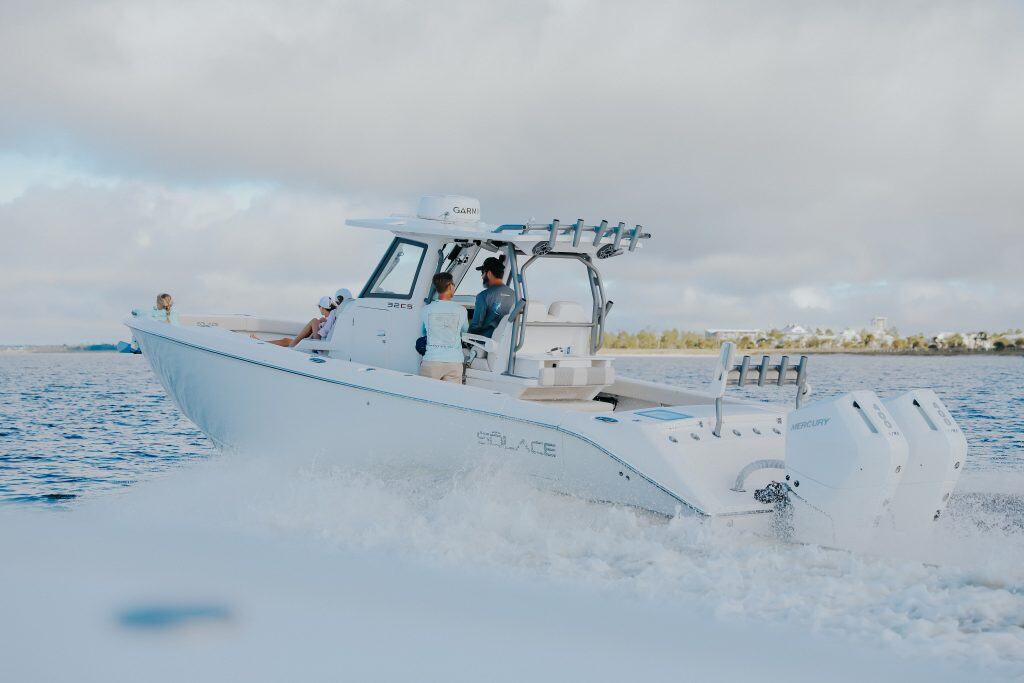 A white motorboat with multiple passengers moves quickly across the water, leaving a wake behind it under a cloudy sky.