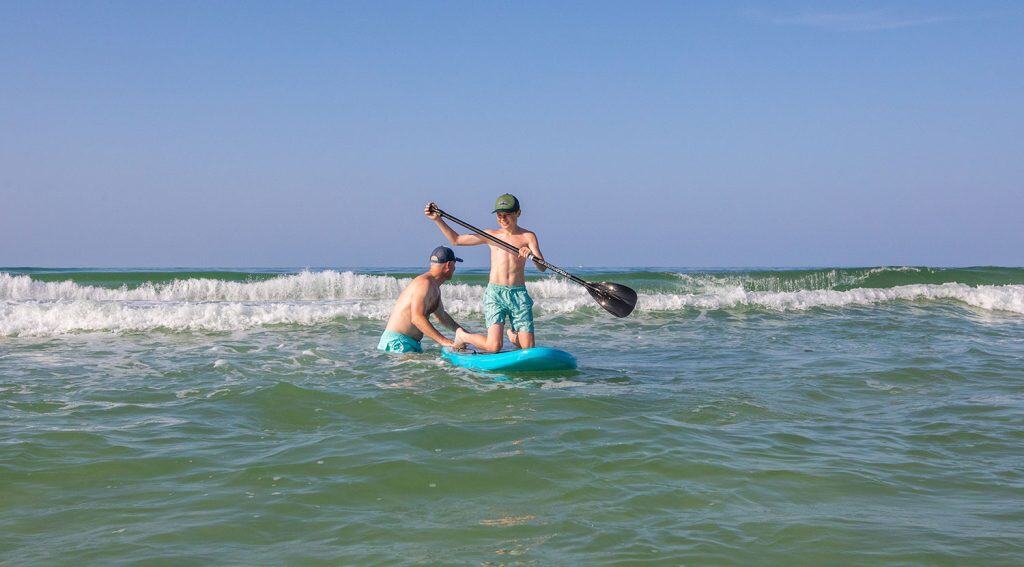 Two people in swimwear are paddleboarding in the ocean near small waves under a clear blue sky.